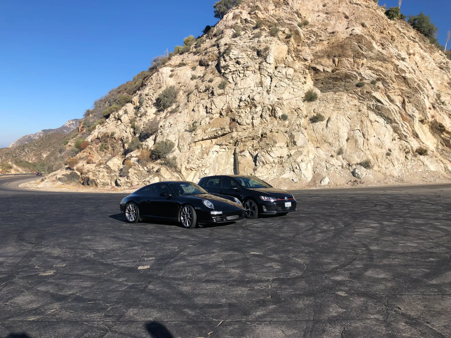 The Stable’s black Porsche Carrera parked beside another car below a rocky mountainside